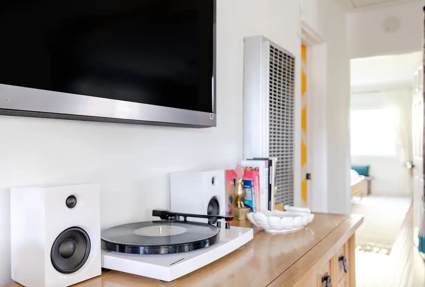 Un salon moderne avec un téléviseur à écran plat fixé au mur, une platine vinyle et un haut-parleur posés sur un meuble en bois.