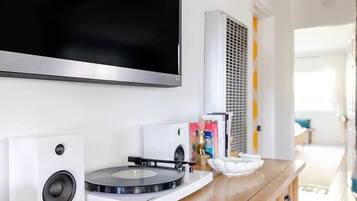 Un salon moderne avec un téléviseur à écran plat fixé au mur, une platine vinyle et un haut-parleur posés sur un meuble en bois.