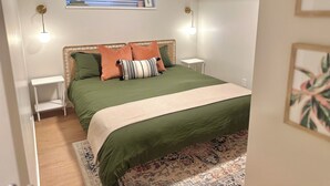A neatly arranged bedroom with a green bedspread, a patterned rug, and a small window with blinds. - Spacious & bright 2 bedroom suite with full kitchen and in-suite laundry!  (Langley Township)