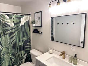 Baño con inodoro, lavamanos y cortina de ducha con estampado de hojas tropicales.