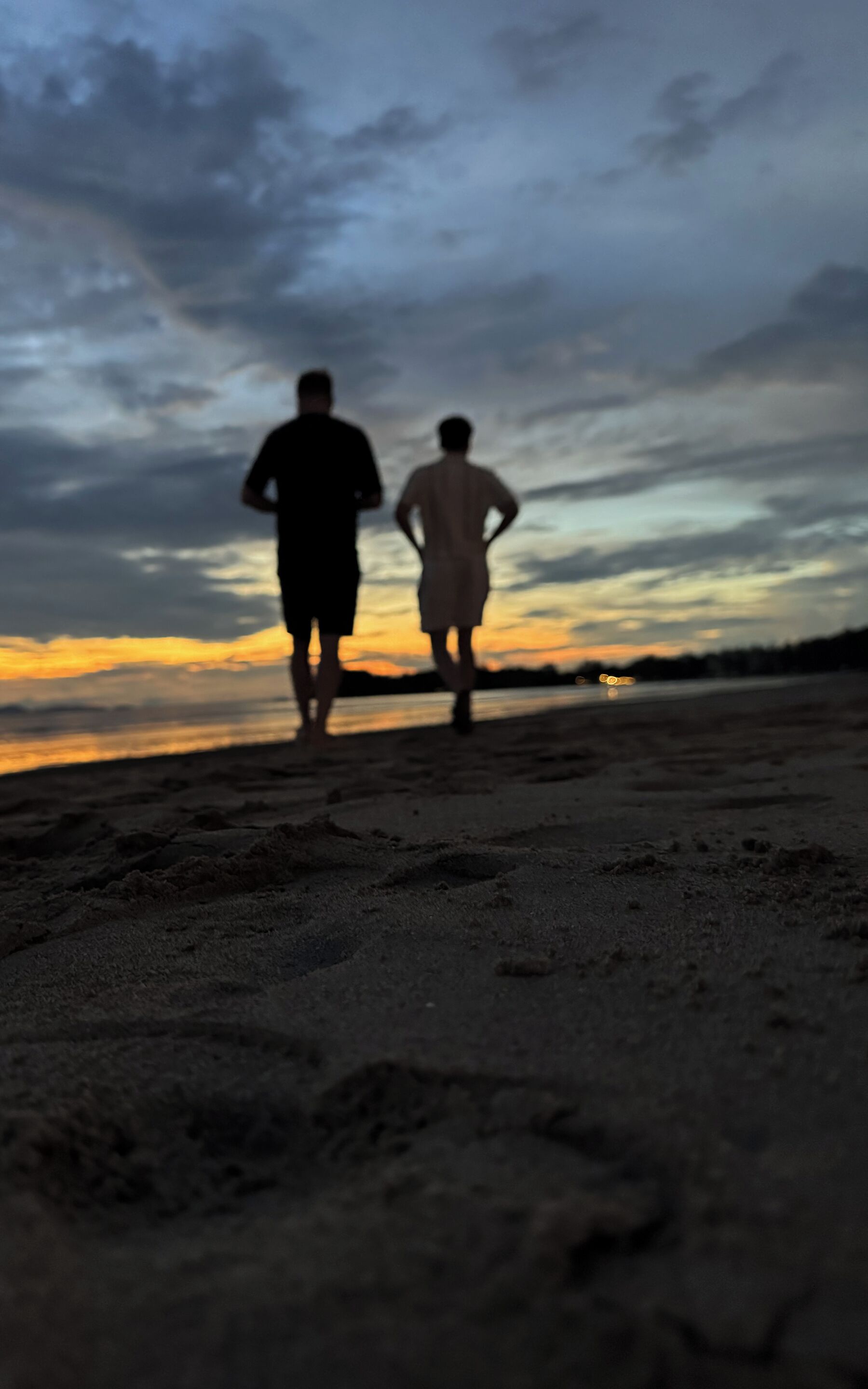 Two people walking on a beach during sunset.