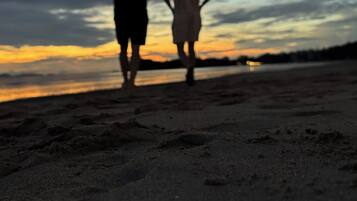 Two people walking on a beach during sunset.