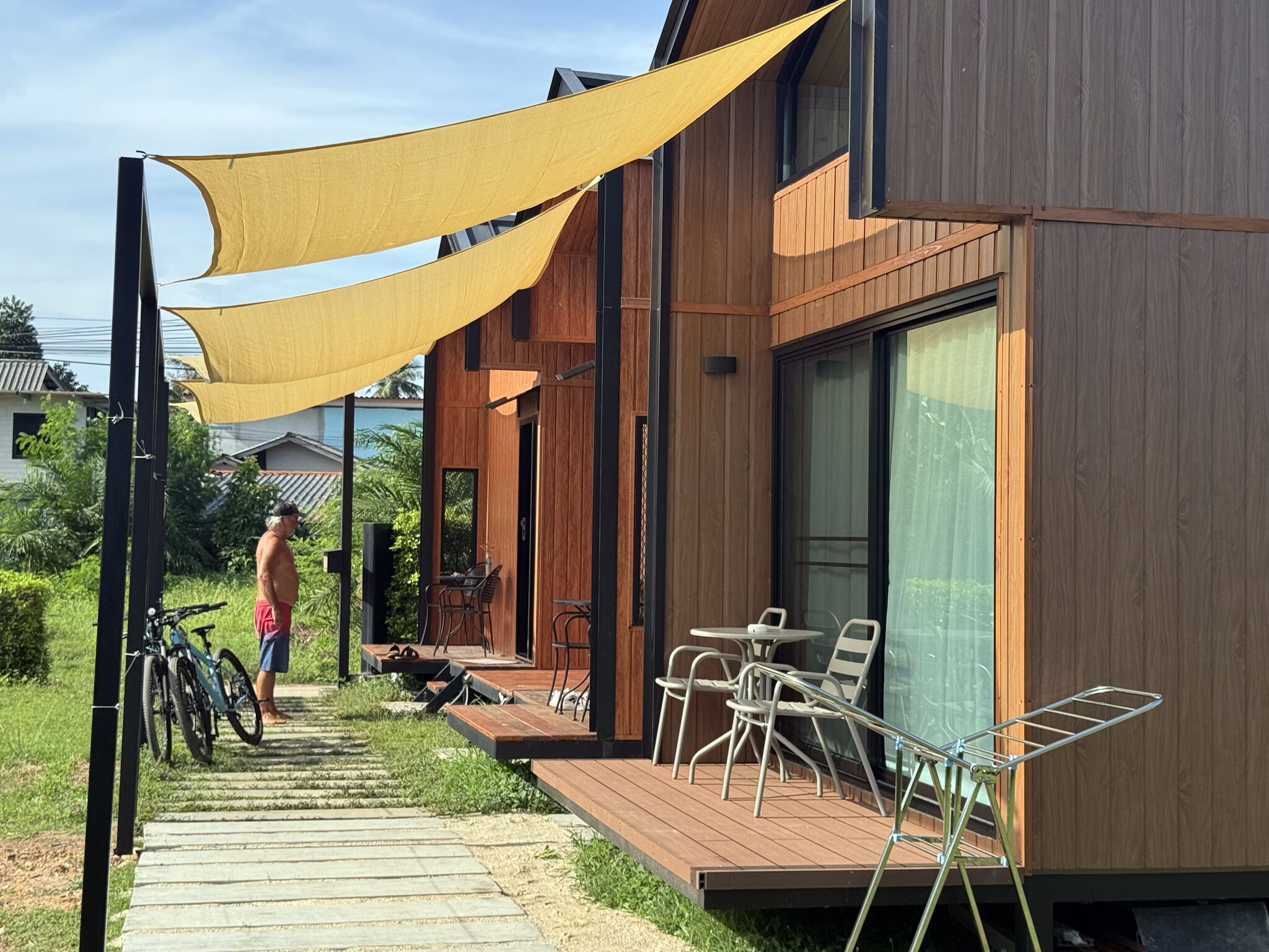 A modern outdoor area with wooden deck, metal chairs, and a yellow shade sail.