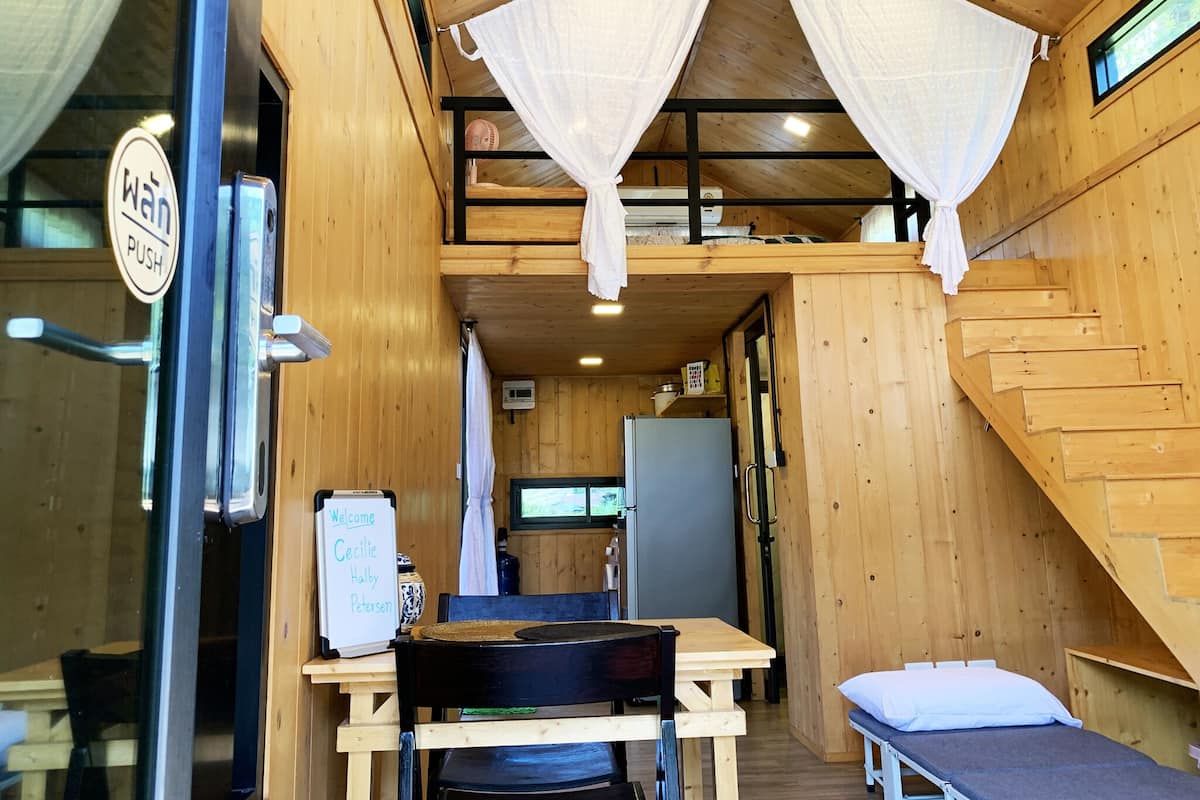 A wooden cabin interior with a bed, a table, and a bench.