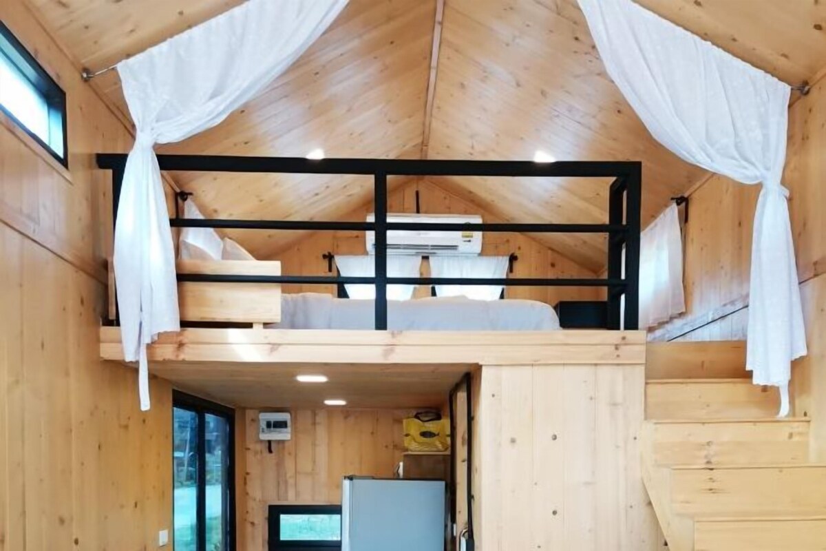 Una cabaña de madera con cama en el altillo, una kitchenette pequeña y una ventana.