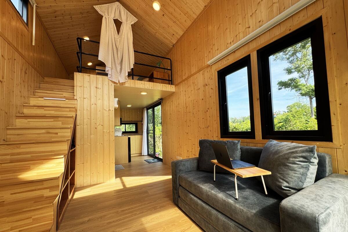 A wooden interior with a sofa, a laptop on a table, and a staircase.