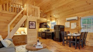 A cozy cabin interior with a staircase leading to a loft, a dining area, and a kitchen with modern appliances. - Romantic Getaway | Hot Tub, Fire Pit, Ping Pong (Richfield)