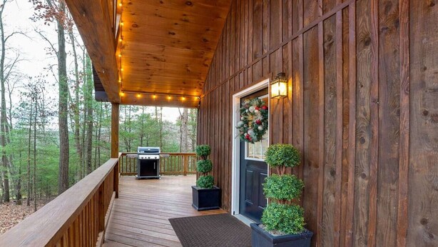 A wooden deck with a barbecue grill, potted plants, and a door with a wreath. - Romantic Getaway | Hot Tub, Fire Pit, Ping Pong (Richfield)