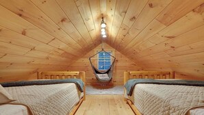 A cozy attic bedroom with wooden walls and floors, two beds with quilts, a hammock, and a hanging light fixture. - Romantic Getaway | Hot Tub, Fire Pit, Ping Pong (Richfield)