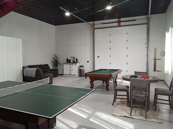 Une pièce équipée d’une table de ping-pong, d’une table de billard et d’une table à manger avec des chaises.