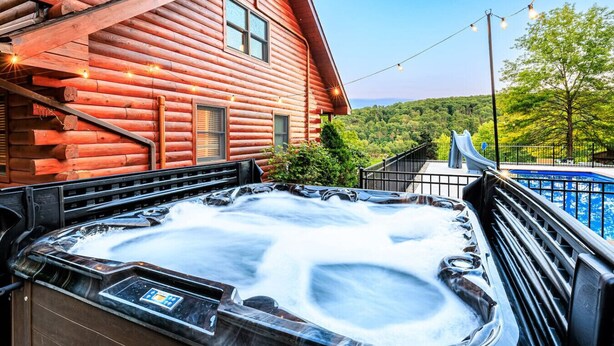 A hot tub with a wooden deck, a red log cabin, and a pool with a slide. - Perfect for couples, families, or small groups, this retreat blends serenity with style for an unforgettable getaway. Plenty of amenities to keep the family entertained indoors and out! (Mount Pleasant Mills)