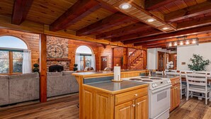 A rustic cabin interior with a wooden dining area, kitchen, and seating by a fireplace. - Perfect for couples, families, or small groups, this retreat blends serenity with style for an unforgettable getaway. Plenty of amenities to keep the family entertained indoors and out! (Mount Pleasant Mills)