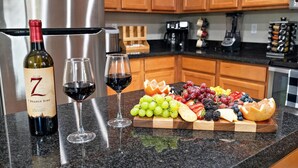 Una encimera de cocina con una botella de vino, dos copas de vino y un plato de fruta.
