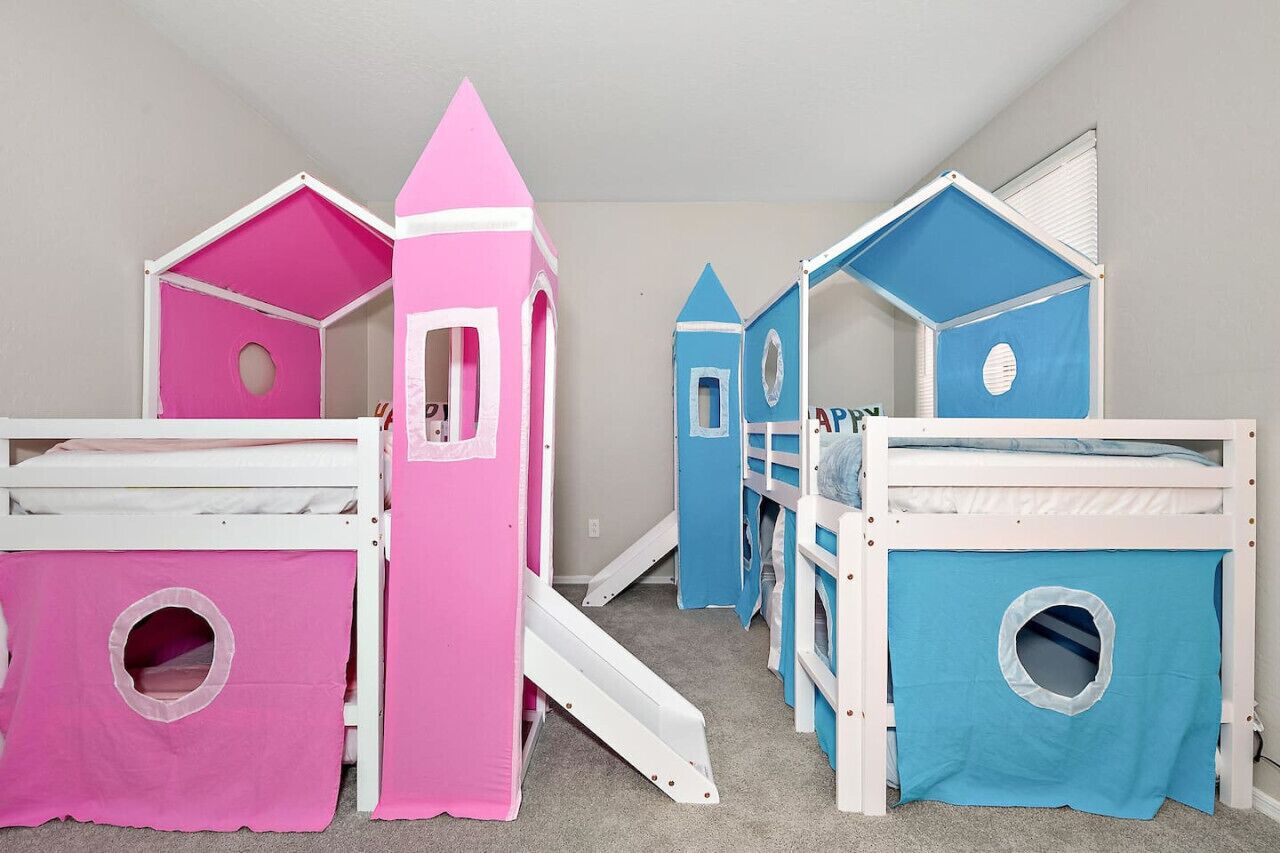Zona de juegos infantiles con literas y casitas de juego en rosa y azul.
