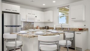 Eine moderne Küche mit weißen Schränken, Granit Arbeitsplatten und Edelstahlgeräten. Vier Barhocker und eine große Kücheninsel mit Spüle sind vorhanden.