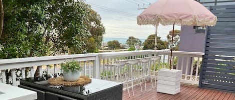 Une terrasse en bois, dotée de mobilier d’extérieur, d’une balustrade blanche et offrant une vue sur la mer.