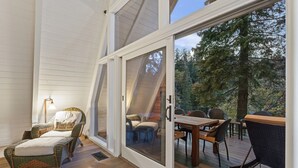 A cozy outdoor seating area with wicker furniture and a wooden deck, overlooking a forested area. - Rocky Point Lakefront | Private Dock & Hot Tub (Lake Arrowhead)