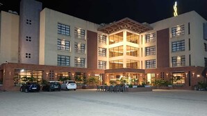 A hotel with a central atrium, multiple floors, and a parking area with cars. - The Pramukh Hotel (Sinor)