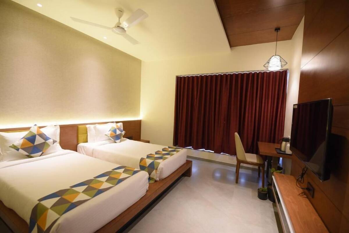 A hotel room with two beds, a ceiling fan, a TV, a desk, and a window with curtains.