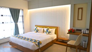 A Deluxe Room with a large bed, a bedside table with a lamp, a chair, and a view of the city through the window. - The Pramukh Hotel (Sinor)