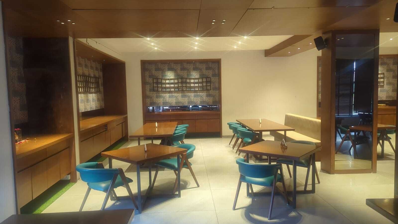 Un comedor moderno con mesas de madera y sillas azules, una pared decorativa y una zona de cocina con armarios de madera.