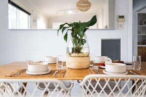 A dining table with white plates, glasses, and a potted plant in the center.