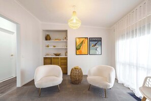 Um interior moderno com dois poltronas brancas, um candelabro, uma cesta decorativa e duas obras de arte emolduradas na parede.