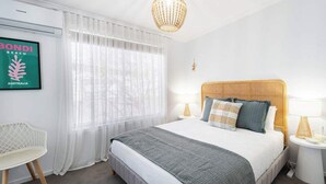 Une chambre à coucher avec un lit, deux tables de chevet, une chaise, un lustre et un tableau encadré au mur.