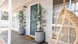 Une véranda avec deux plantes en pot, une porte bleue et une chaise en osier.