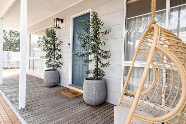 A porch with two potted plants, a blue door, and a wicker chair.