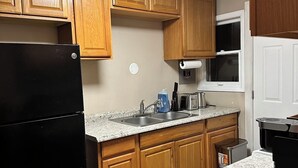 A kitchen with wooden cabinets, a black refrigerator, a sink, and a microwave.