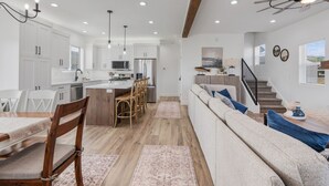 Una cocina moderna con armarios blancos, una isla central con taburetes y un área de comedor con una mesa y sillas de madera.
