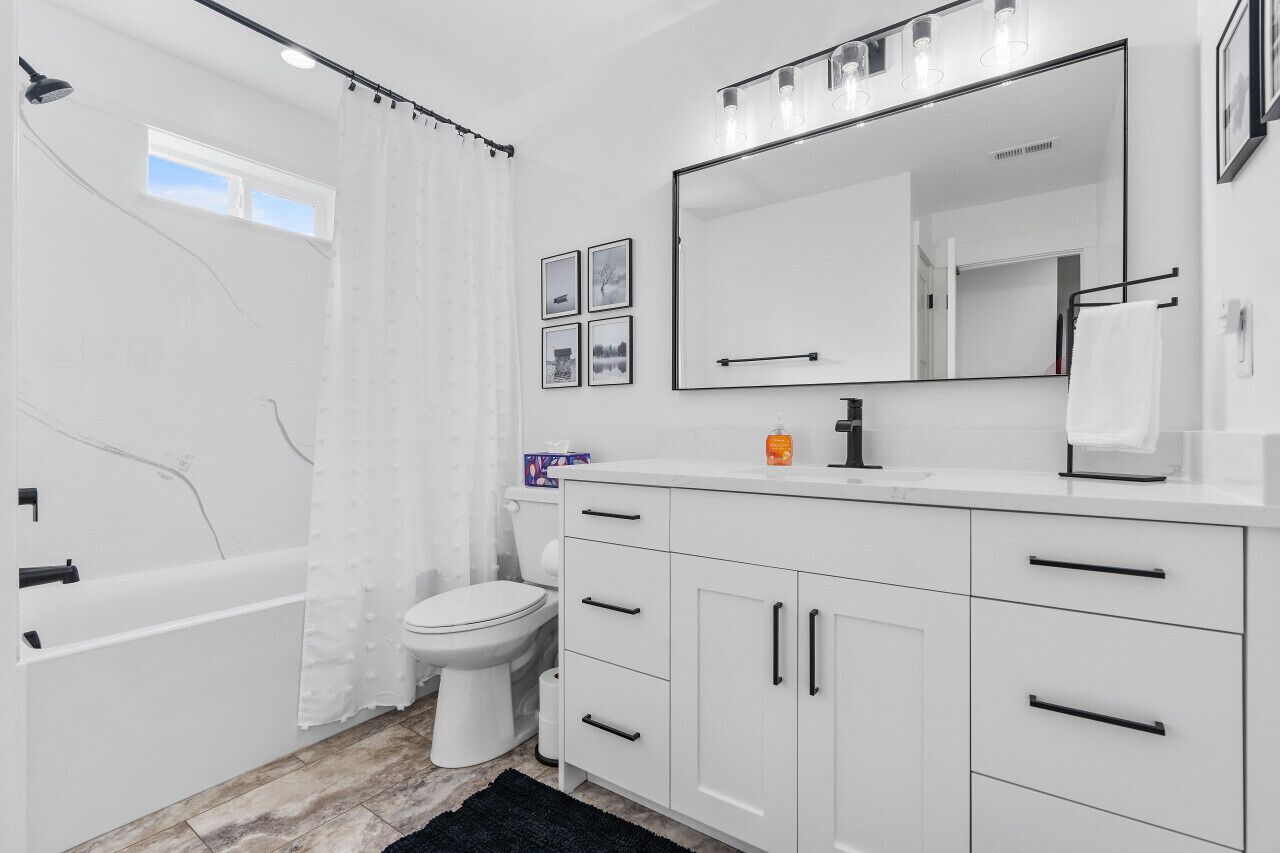 A modern bathroom with a bathtub, toilet, and vanity with a large mirror.