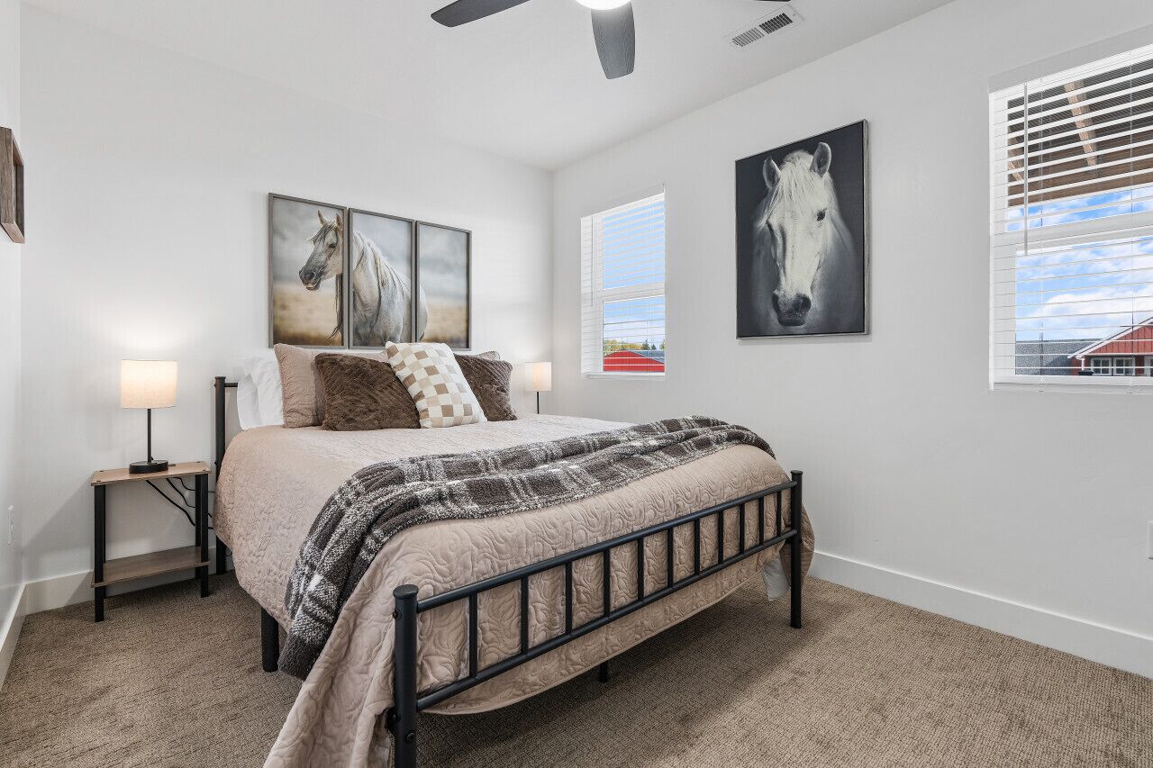 Une chambre à coucher avec un lit, une table de chevet, une lampe et deux tableaux sur le thème des chevaux accrochés au mur.