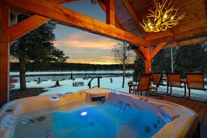Een bubbelbad met uitzicht op een besneeuwd meer en bos bij zonsondergang.