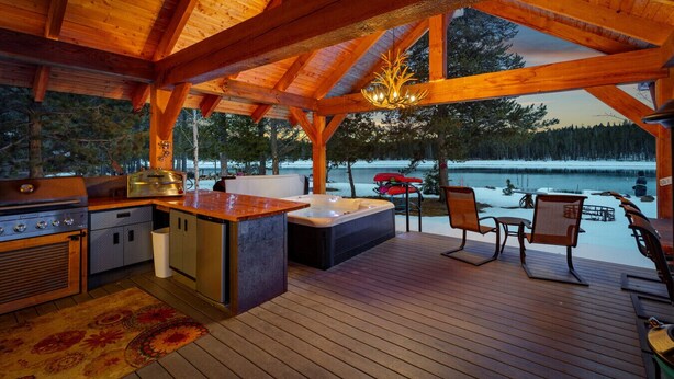 Een houten terras met een keukenhoek, inclusief een barbecue en een jacuzzi, met uitzicht op een besneeerd landschap.