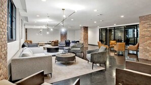 Un espace de détente moderne, doté de canapés, de fauteuils et d’une table basse, avec des murs en briques apparentes et de grandes fenêtres.