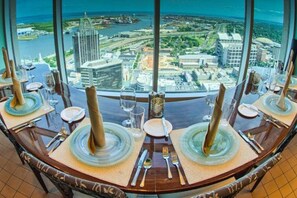 Een eettafel met borden, bestek en glazen, met op de achtergrond een stadsgezicht en uitzicht op water.