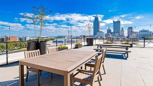 Un espace extérieur aménagé avec des tables et des chaises, des plantes en pot, et une vue sur les bâtiments de la ville en arrière-plan.