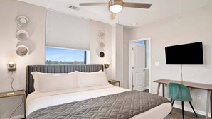 Une chambre d’hôtel moderne dotée d’un grand lit, d’un bureau avec une chaise, d’un ventilateur de plafond et d’un téléviseur fixé au mur.