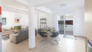 A modern living room with a sofa, a dining table with chairs, and a kitchen area. - Protaras Blue River Villa Br26 (Περνέρα)