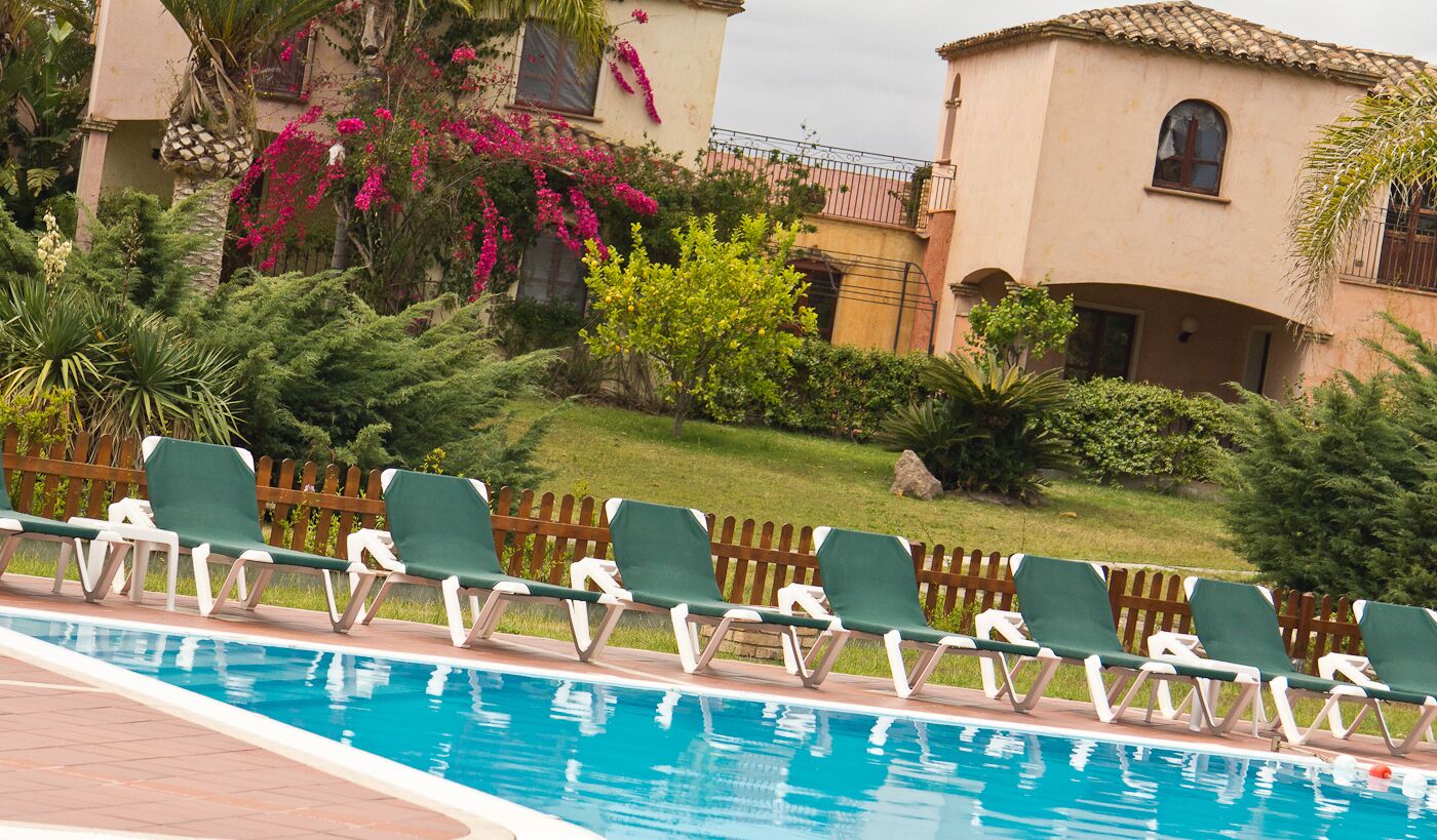 A pool area with lounge chairs and a sign reading "Baia delle Palme Albergo Residenziale".