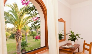Una habitación con ventana a un jardín, una mesa de madera con una silla y una planta en maceta.