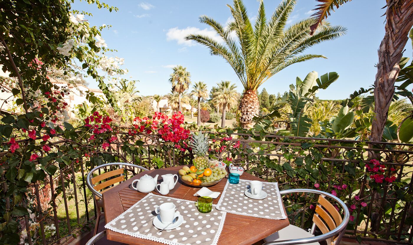 An outdoor dining area with a table set for two, surrounded by lush greenery and a variety of tropical plants.
