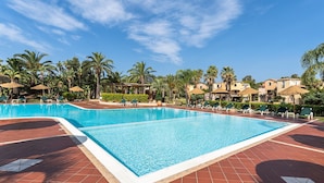 A rectangular swimming pool with a tiled deck, surrounded by palm trees and lounge chairs.