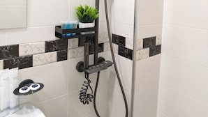 Un baño moderno con ducha, un estante pequeño con artículos de aseo y una planta en maceta.
