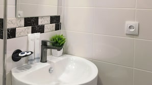 Un baño con un lavamanos blanco, un espejo, un perchero para toallas, una planta en maceta y un salpicadero de azulejos de mármol.