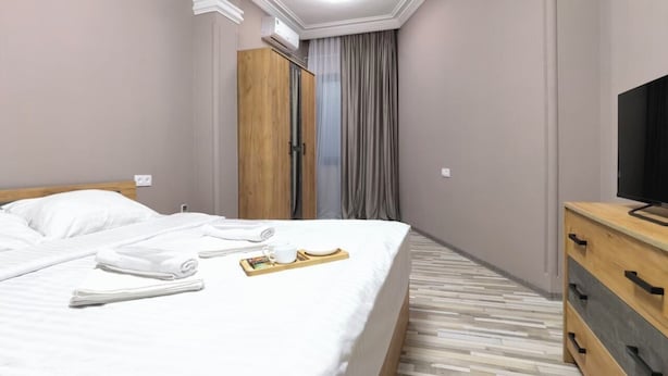 Una habitación de hotel con una cama, un aparador de madera, un televisor y una ventana con cortinas.
