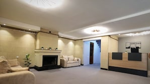 Vestíbulo de hotel con chimenea, sofás, mostrador de recepción y una escalera que lleva a otra zona.