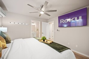A bedroom with a bed, a ceiling fan, a TV displaying "ROKU", and a bathroom visible through an open door. - Urban Oasis in the Heart of Sacramento! (Sacramento)